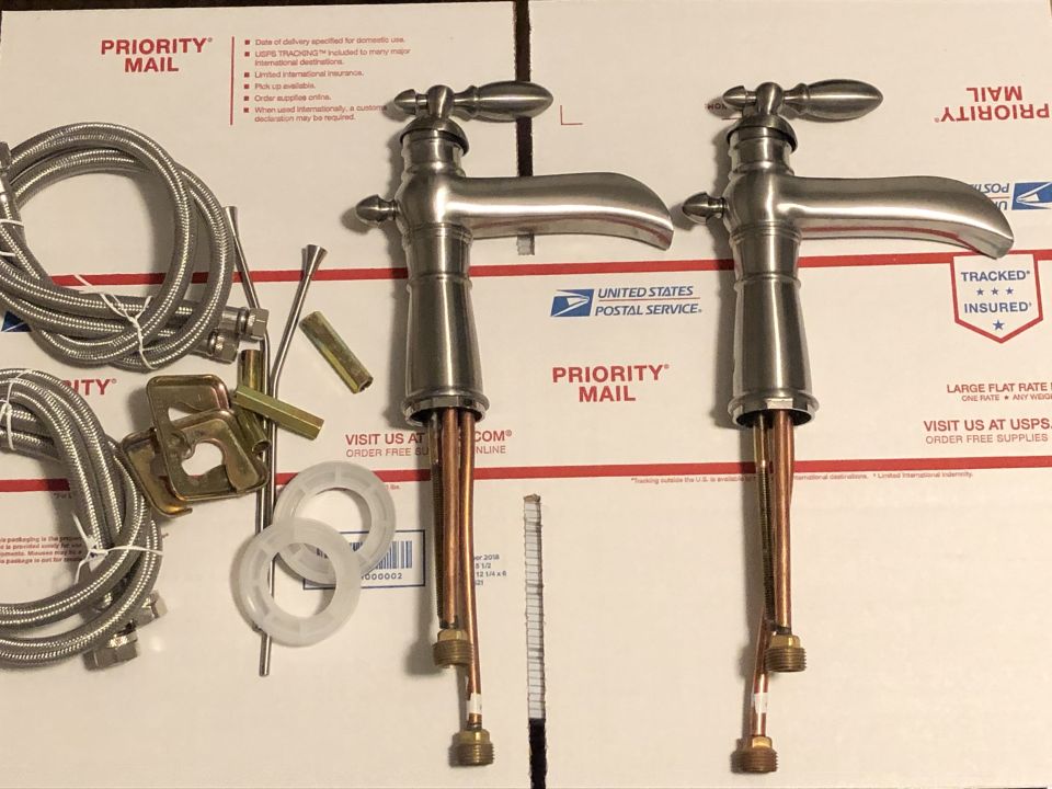 Two new faucets and plumbing parts laid out on Priority Mail boxes