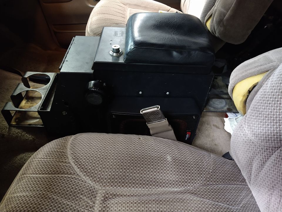 Interior shot of a vehicle's center console with cup holders, armrest, and a speaker grille