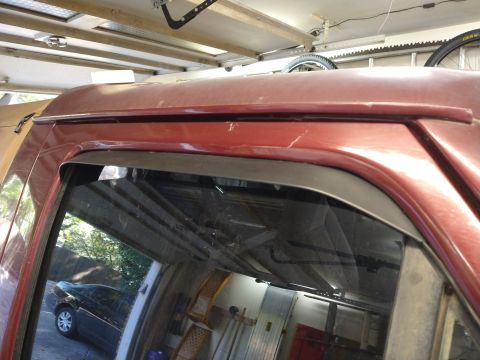1996 Ford Bronco - Close-up of a red SUV's roofline and window, showing an in-channel rain guard and reflections in the glass.