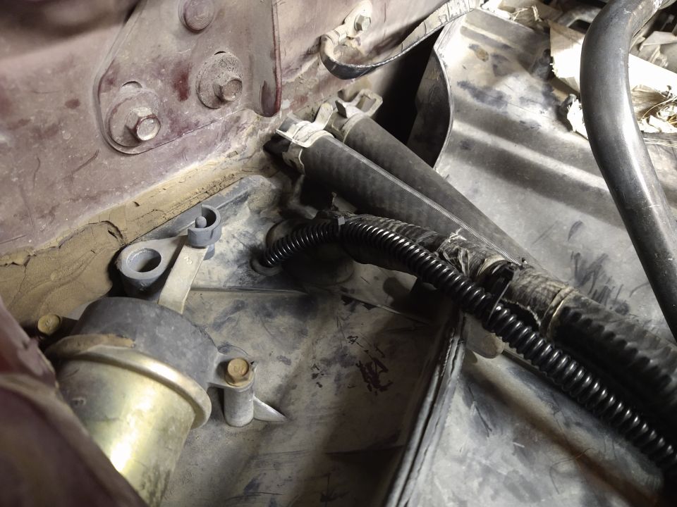 Engine bay with hoses, wiring, and a vacuum actuator. The area is dusty and shows signs of wear
