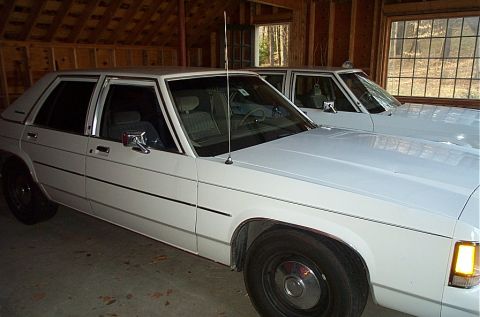 1991 Ford LTD Crown Victoria - Two white sedans are parked side-by-side in a wooden garage.
