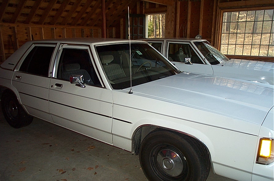 White sedan parked in a garage, front quarter view. Another white sedan is visible behind it