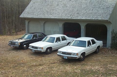 1991 Ford LTD Crown Victoria - Three white 1991 Ford Crown Victorias and one black Ford Crown Victoria are parked in front of a garage.