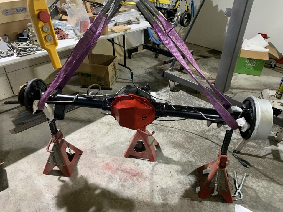 Rear axle assembly suspended by straps and resting on jack stands in a garage
