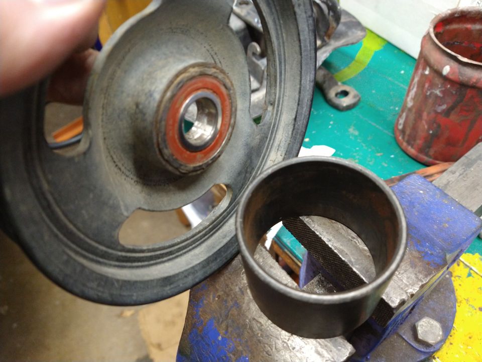 Close-up of a vehicle pulley with bearing and a metal sleeve in a vise.