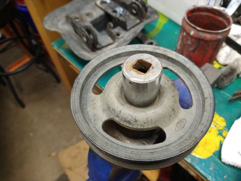 1996 Ford Bronco - A close-up shot shows a metal pulley with a square opening in the center, held in a blue vise. The pulley is resting on a colorful, worn wo…