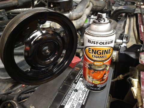 1996 Ford Bronco - A black pulley, possibly recently painted with black engine enamel, sits on top of a car battery in an engine bay. A can of Rust-Oleum Engi…
