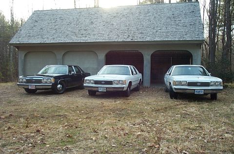 1991 Ford LTD Crown Victoria - Three Ford Crown Victorias from the 1980s are parked in front of a three-bay garage.