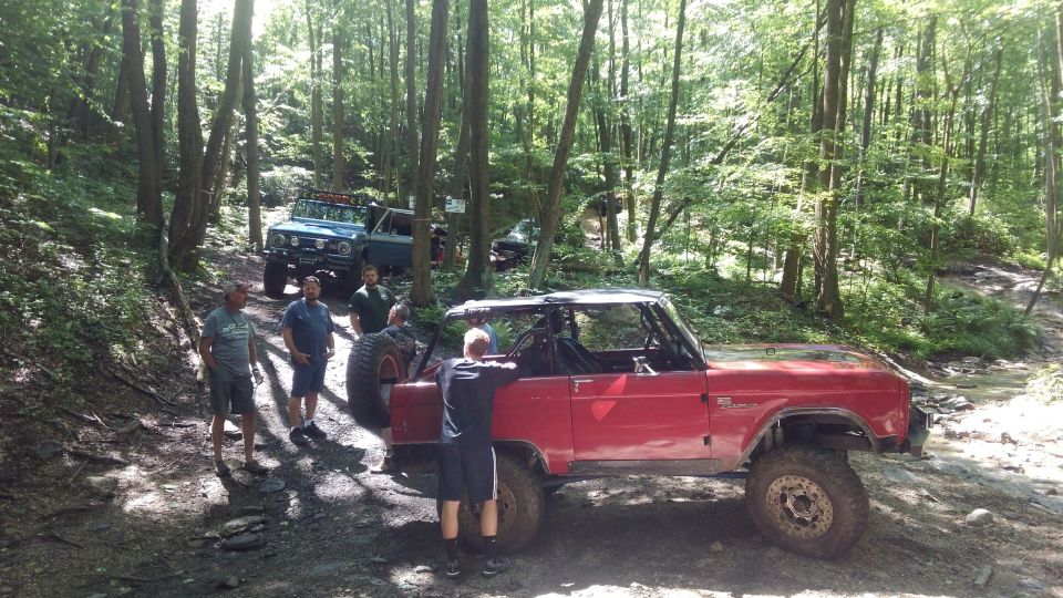 Red Ford Bronco with top removed and a group of people standing around it in a wooded area.