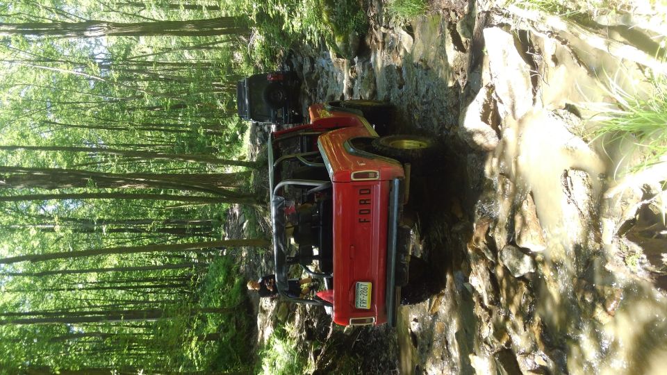 Red Ford Bronco off-roading on a muddy, rocky trail in a forest.