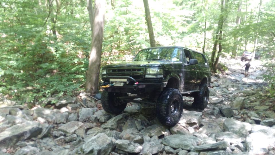 Black Ford Bronco off-roading on a rocky trail in a forest.