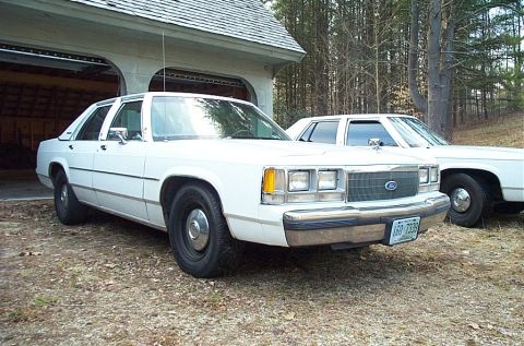 1991 Ford LTD Crown Victoria - A white 1991 Ford Crown Victoria LTD is parked in front of a garage, with another white sedan visible behind it.