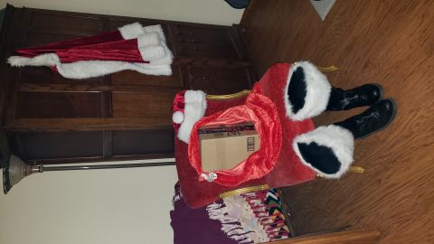 1965 Ford Mustang - A person dressed as Santa Claus is sitting in a red chair with a sack of gifts. A Santa hat is on the chair and a red coat with white trim…