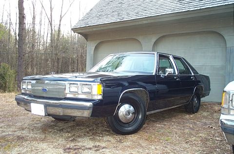 1991 Ford LTD Crown Victoria - A 1991 Ford Crown Victoria LTD is parked outside a garage, with another vehicle to its right.