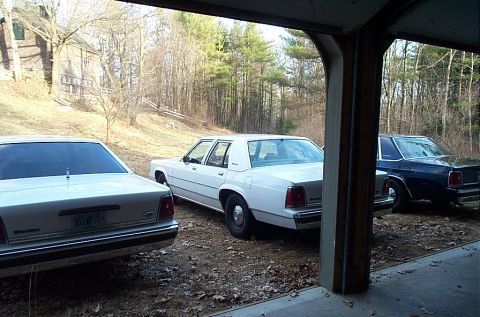 1991 Ford LTD Crown Victoria - A white 1991 Ford Crown Victoria LTD is parked under a garage with two other sedans visible.