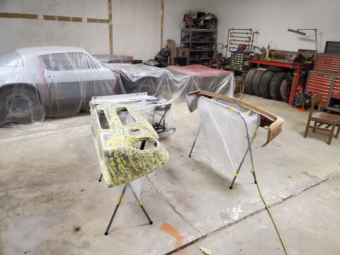 1979 Chevrolet Camaro - Multiple vehicles are covered in plastic in a workshop, with car parts on stands in the foreground.