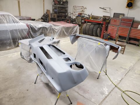 1979 Chevrolet Camaro - Car parts, including a front bumper and fender, are prepped for painting in a workshop setting, with other vehicles covered in plastic.