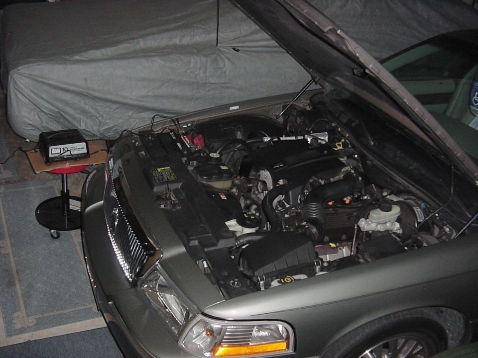 Engine bay of a gray car with hood open beside a covered vehicle in a garage