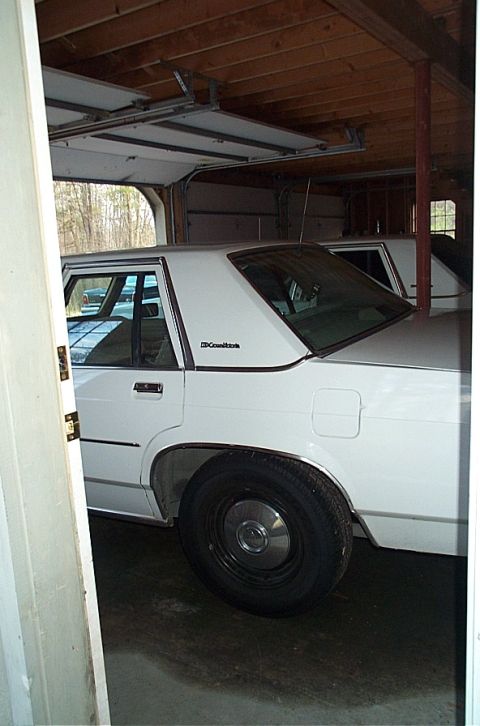1991 Ford LTD Crown Victoria - A white sedan is parked in a garage, with another vehicle visible behind it.