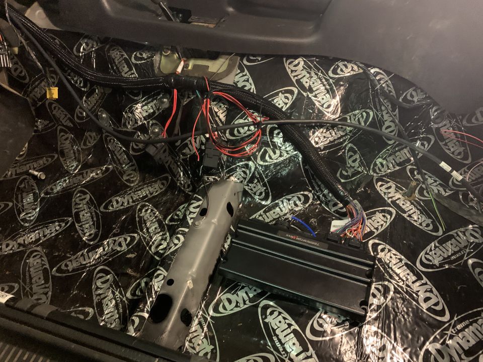 Car interior floor covered in Dynamat sound dampening, with exposed wiring and an amplifier