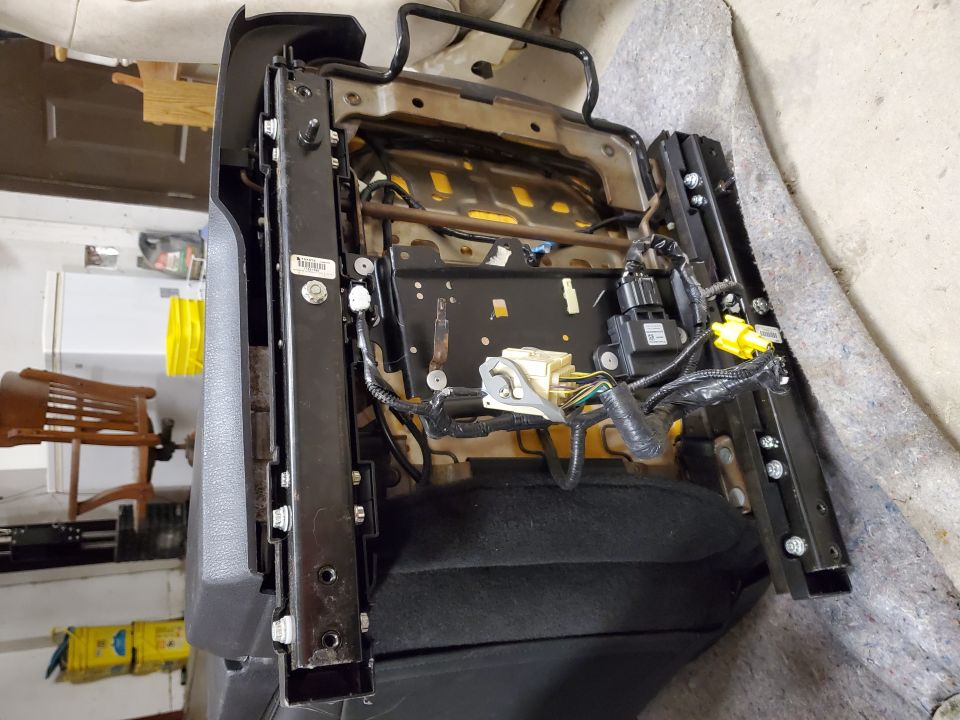 Car seat frame with exposed wiring and metal rails, viewed from the side