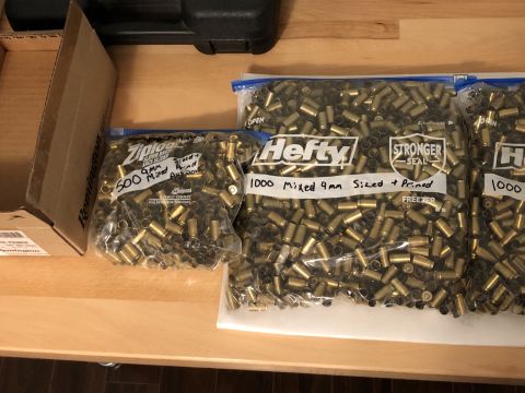 1995 Mercury Grand Marquis - Bags of spent 9mm ammunition casings are organized and labeled on a wooden table, with a cardboard box nearby.