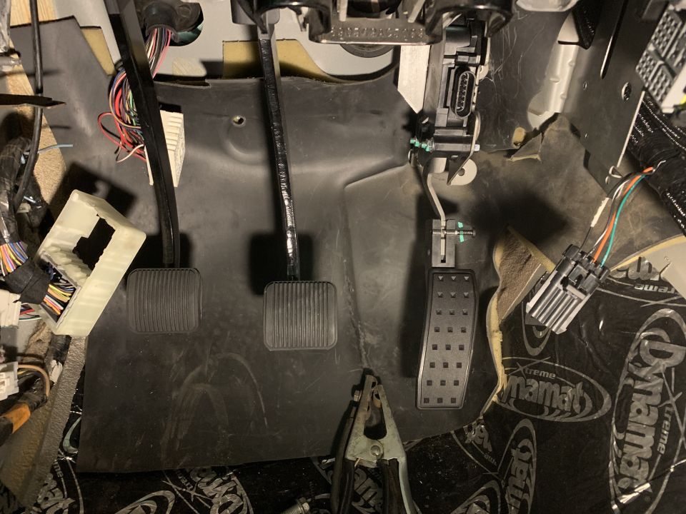Vehicle interior footwell with brake and accelerator pedals, exposed wiring, and sound dampening material