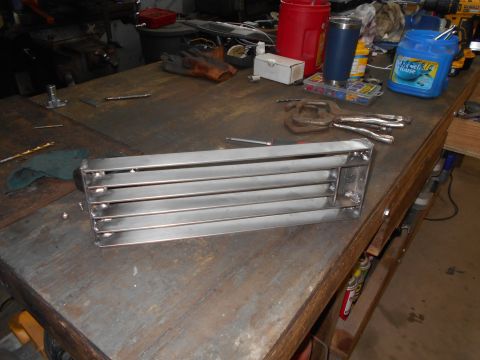 1992 Ford Bronco - A metal grille part sits on a workbench next to various tools and containers.