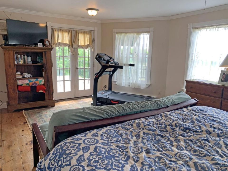 Bedroom with a treadmill, TV on a bookshelf, and double doors leading outside