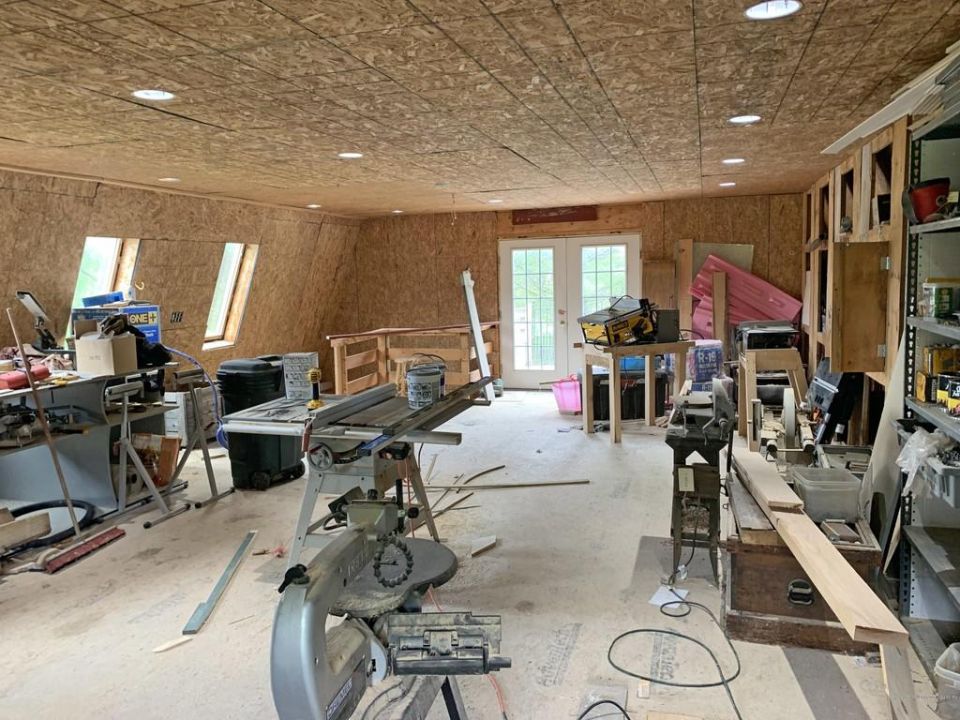 Workshop interior with table saw, miter saw, and other woodworking tools. Double doors lead outside