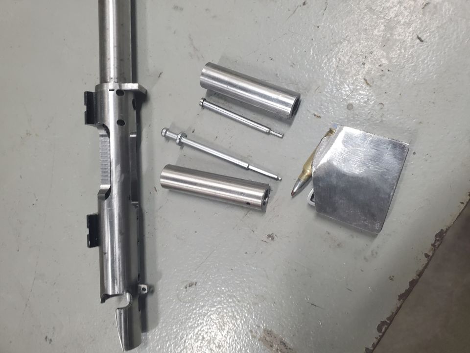 Gun bolt assembly and related components on a gray floor. A Supermotors.net watermark is visible