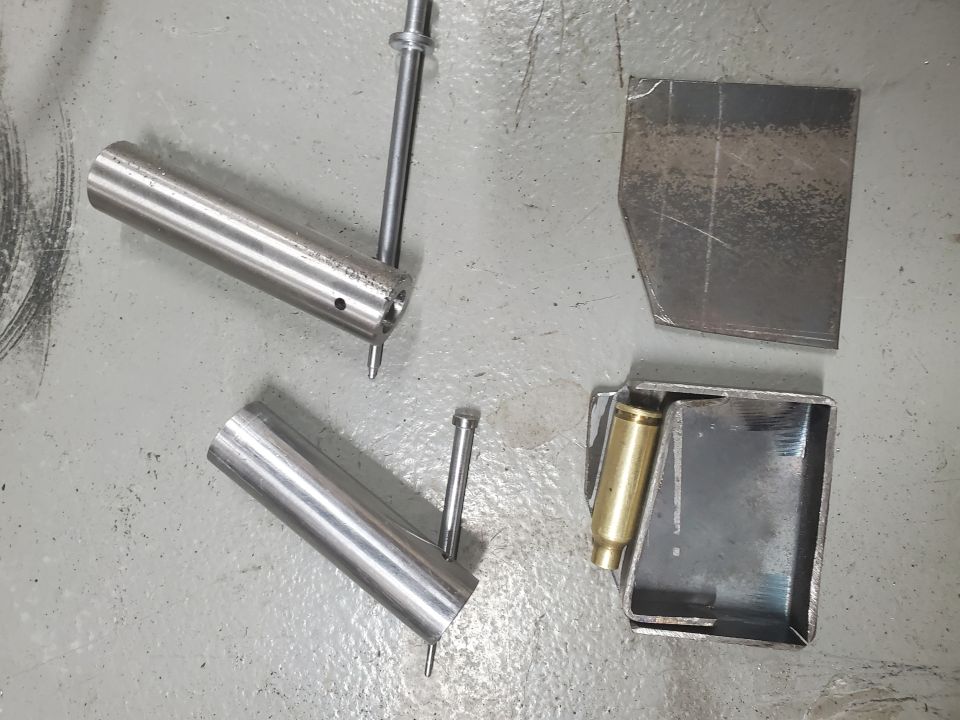 Metal tubes, a metal bracket, and a brass casing on a concrete floor