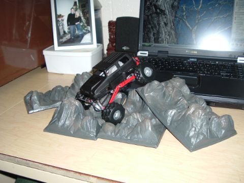1989 Ford Bronco - A black remote control rock crawler toy truck navigates a set of gray rock obstacles on a desk.