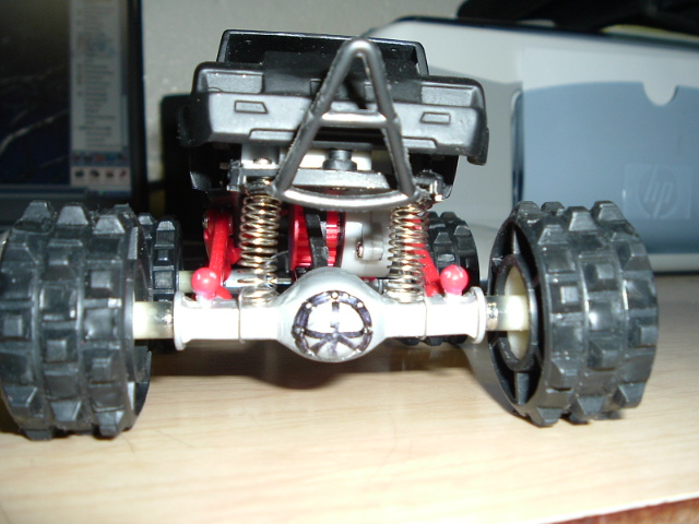 Toy monster truck model showing rear axle, coil springs, and dual knobby wheels on a desk