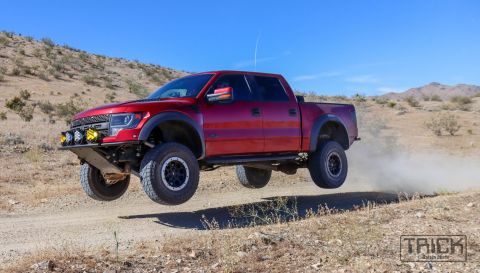 2014 Ford F-150 - This red pickup truck is airborne, kicking up dust on a desert trail.