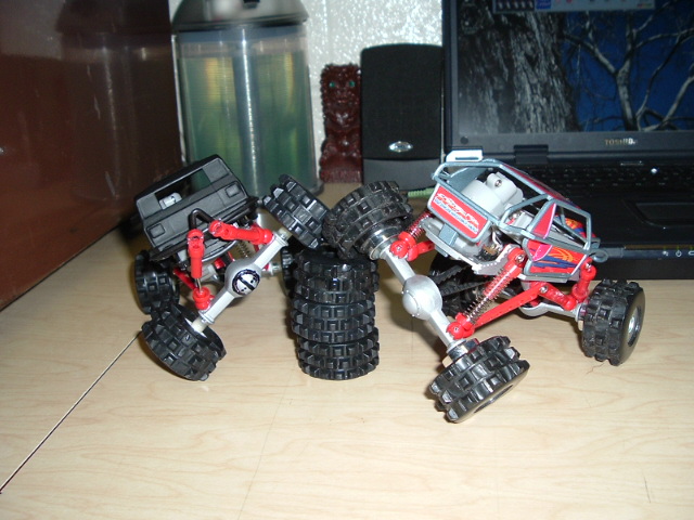 Two toy rock crawler trucks with spare tires on a desk next to a laptop