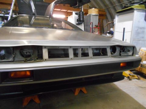 1992 Ford Bronco - A silver DeLorean DMC-12 sits in a workshop, its front end disassembled and gullwing doors ajar.