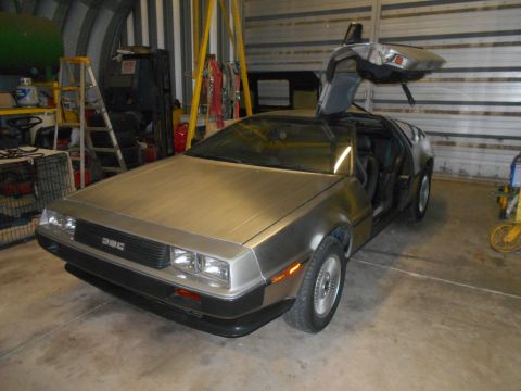 1992 Ford Bronco - Silver DeLorean DMC-12 with gullwing doors open, parked inside a garage.