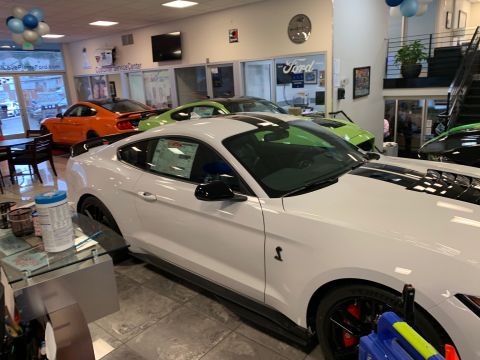 2020 Ford Mustang - A white Ford Mustang Shelby GT500 is displayed prominently in a dealership showroom, alongside other colorful Ford Mustangs.
