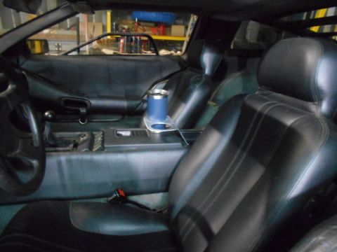 1992 Ford Bronco - Interior view of a car's black leather seats and center console, with a blue cup holder visible.