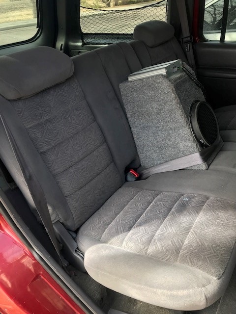 2000 Ford Explorer - The interior of a red SUV shows gray patterned rear seats and a subwoofer box.