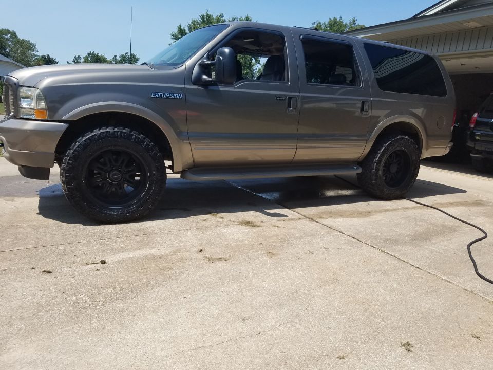 Brown 2003 Ford Excursion with black rims and off-road tires parked on a driveway