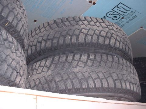 2003 Ford Excursion - Several off-road tires are stacked on a shelf, showing their deep tread blocks.