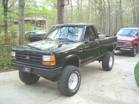 1989 Ford Ranger - This lifted Ford Ranger has large off-road tires and a lifted suspension. Another vehicle is parked behind it.