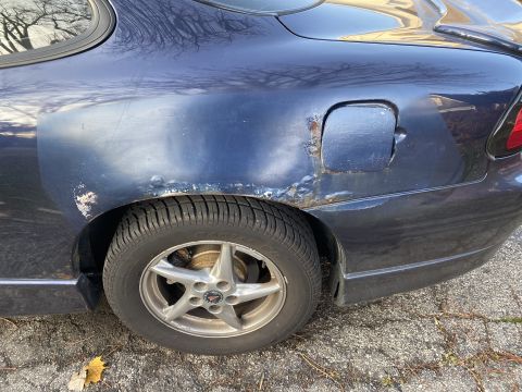 2000 Pontiac Grand Prix - Rear quarter panel of a dark blue 2000 Pontiac Grand Prix shows significant rust around the wheel well and fuel door.