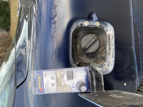 Close-up of a car's open fuel filler door with a package of neodymium magnets placed in front of it