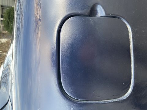 Dark blue fuel door on a car's body panel, with a slight reflection of trees and sky