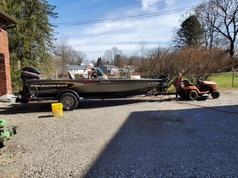 2005 Tracker Tournament - A Tracker boat is parked on a gravel driveway next to a riding mower.
