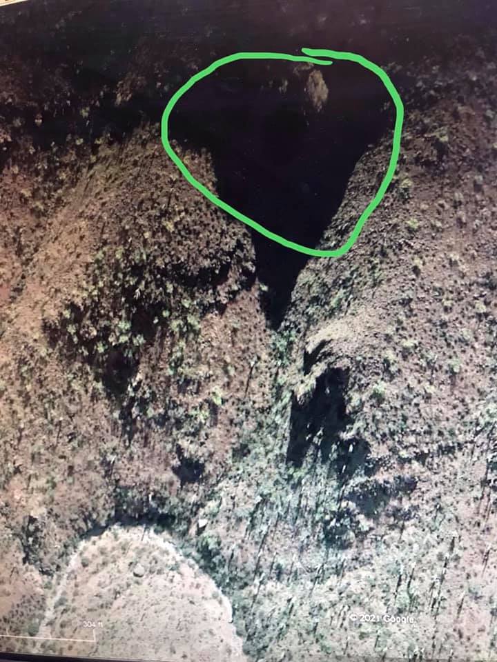 Aerial view of a dark canyon with scrub brush and rocky terrain. A green circle highlights a shadowed area within the canyon