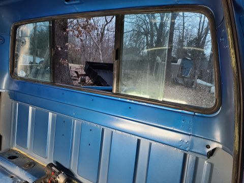 1995 Ford F-150 - View from inside a blue truck cab, showing the interior paneling and the exterior scene through the rear window.